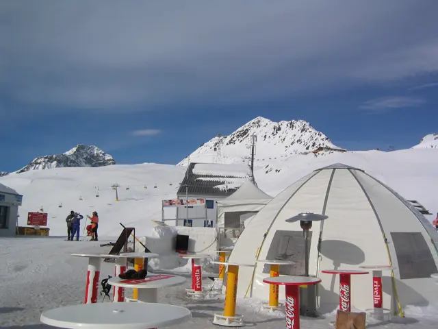 A dome-shaped terrace structure and bright table supports sit below a snowy summit.
