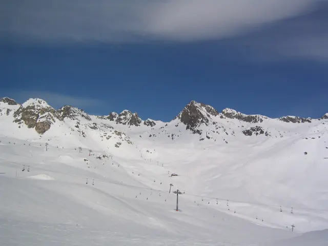 Jagged rocky peaks line a broad white basin crossed by ski lifts.