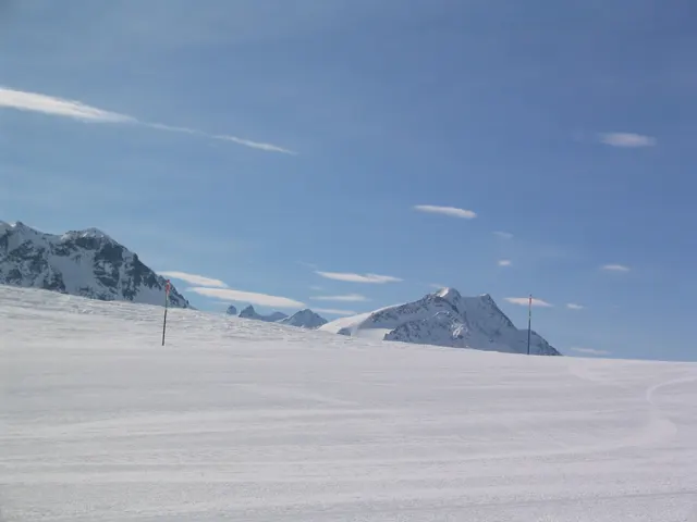 A broad snowy plateau stretches toward distant peaks beneath wisps of cloud.