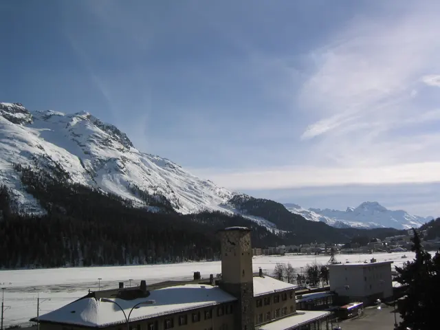 A station tower and snowy roofs sit below a mountain slope and wispy clouds.