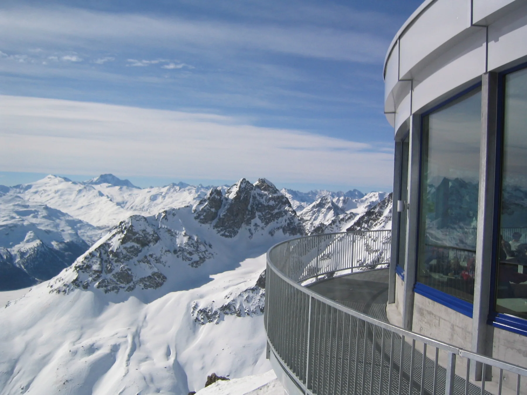 A curved balcony follows a glazed building above jagged snow-covered peaks.