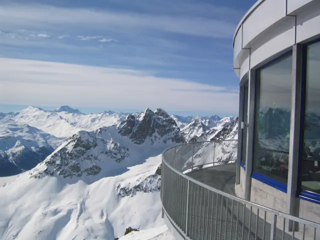 A curved balcony follows a glazed building above jagged snow-covered peaks.