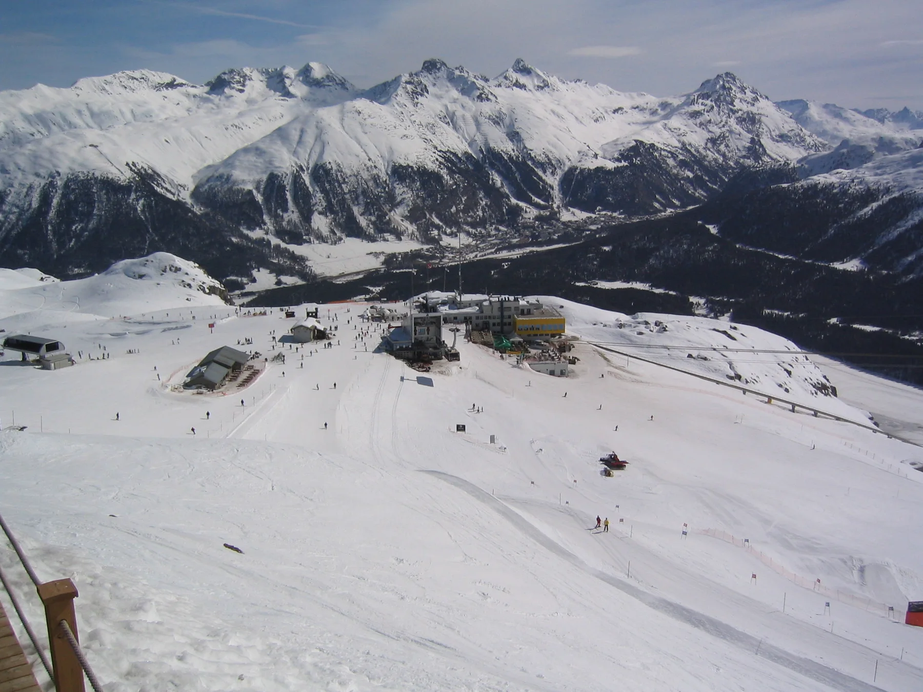 Broad ski runs descend toward a mountain valley beneath a wide snowy range.