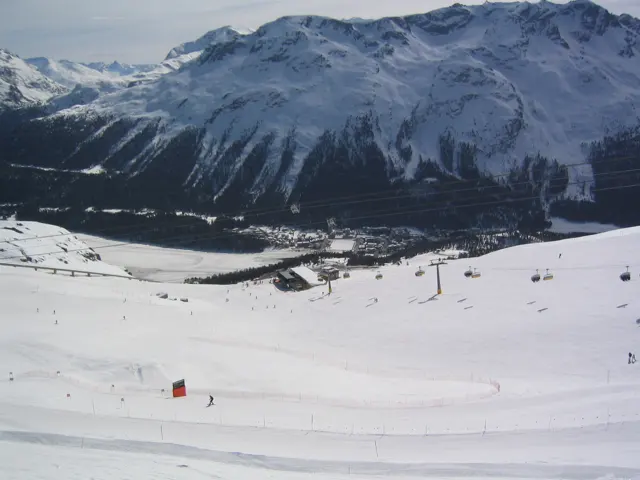 A snowy slope overlooks a deep valley below a steep snow-covered mountain wall.