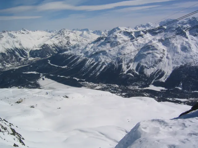 A high snow-covered slope overlooks a dark valley enclosed by snowy mountains.
