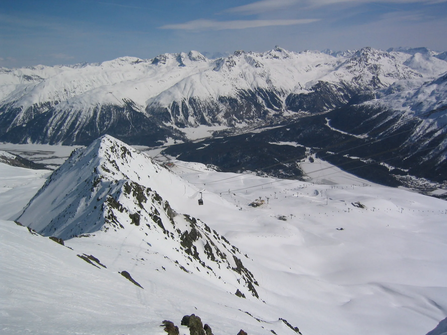 A pointed snow-covered ridge rises before a broad mountain valley and distant peaks.