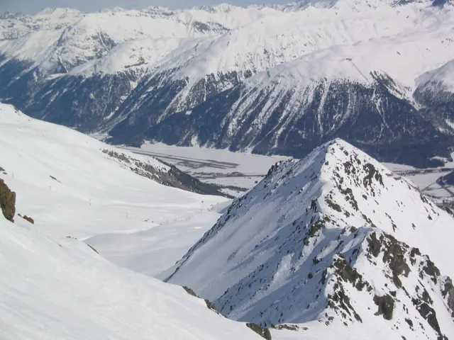 A narrow ridge with exposed rocks divides the snowy foreground above a deep valley.