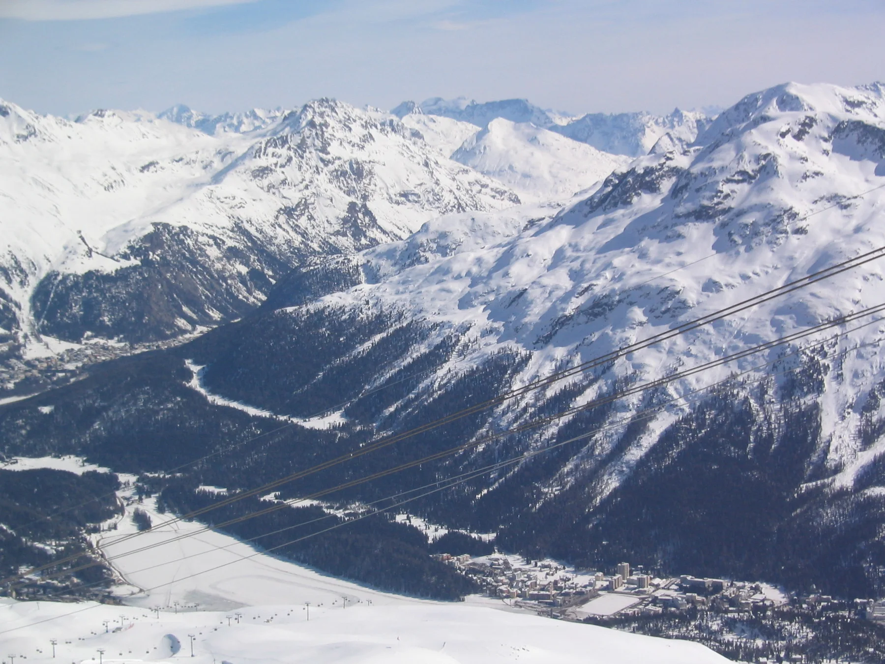 A high snowfield overlooks a valley and layers of steep snowy mountains.