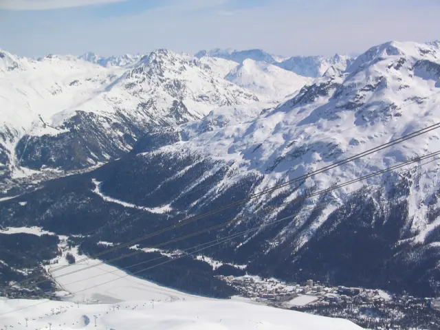 A high snowfield overlooks a valley and layers of steep snowy mountains.