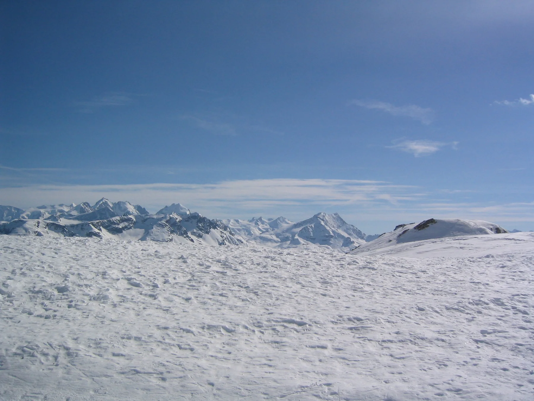 Rough, sparkling snow fills the foreground beneath a distant line of peaks and blue sky.